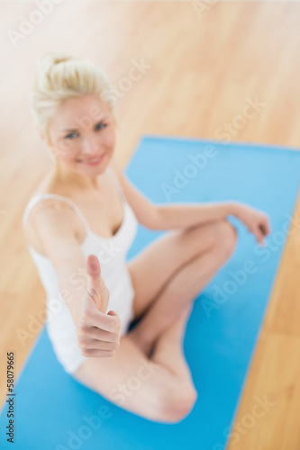 Toned woman gesturing thumbs up on exercise mat at fitness studi