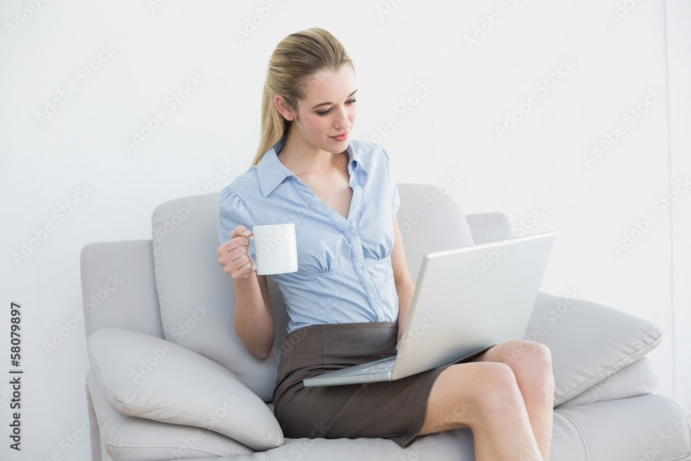 Lovely calm businesswoman using her notebook holding a cup Lovely calm businesswoman using her notebook holding a cup