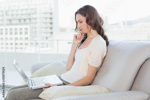 Side view of a casual young woman using laptop on sofa