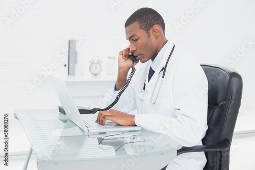 Male doctor using phone and laptop at medical office
