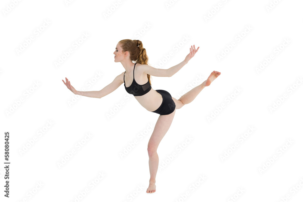 Side view of a sporty young woman standing on one leg