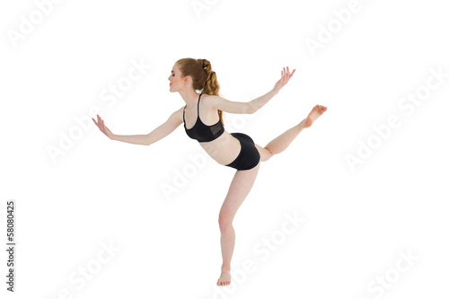 Side view of a sporty young woman standing on one leg