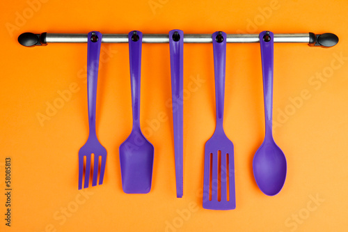 Plastic kitchen utensils on silver hooks on orange background