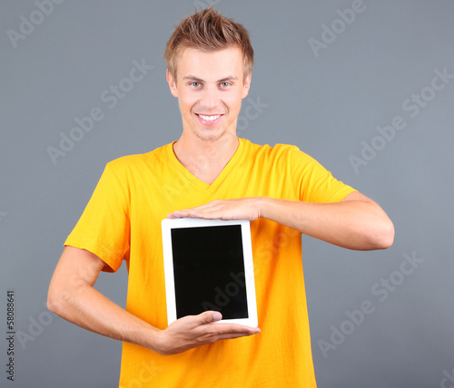 A handsome young man with tablet on grey background