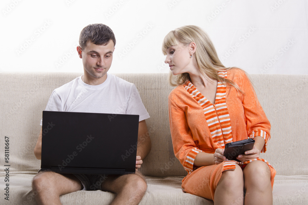 Парень с ноутбуком сидит на диване, девушка с планшетом смотрит Stock Photo