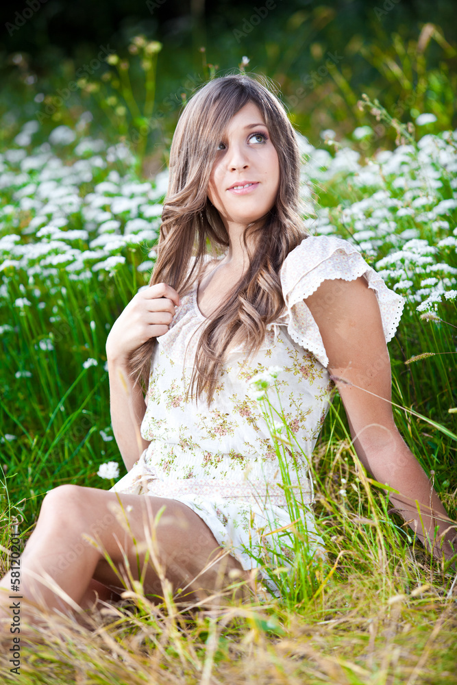 Sexy young woman sitting on meadow and touching her long hair Sexy young woman sitting on meadow and touching her long hair