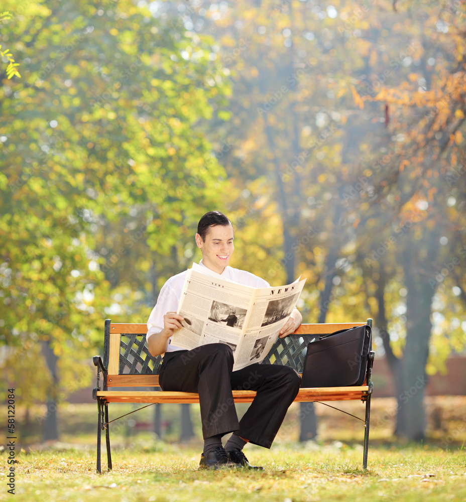 Businessman seated on a bench reading a newspaper in a park