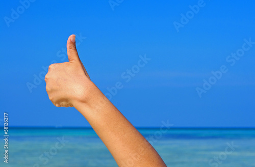 Hand with thumb up on blue sky and sea background