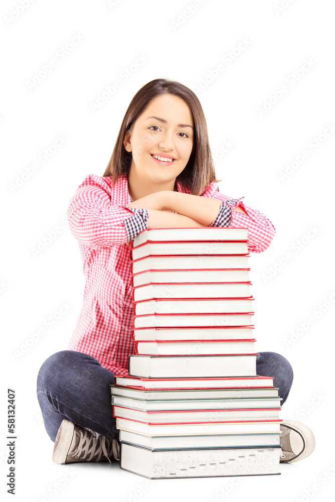 Smiling young female student sitting next to a pile of books Smiling young female student sitting next to a pile of books