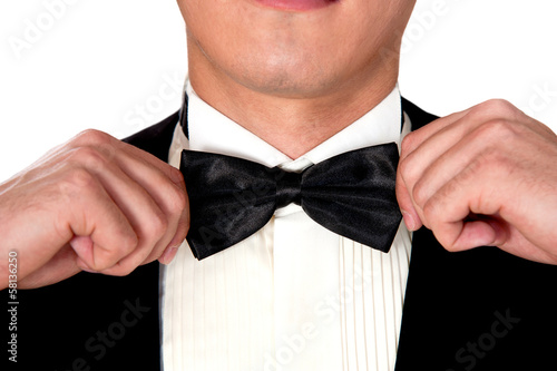man in a black suit adjusts his bow tie close-up face