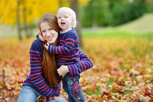 Young mother and toddler girl have fun at autumn