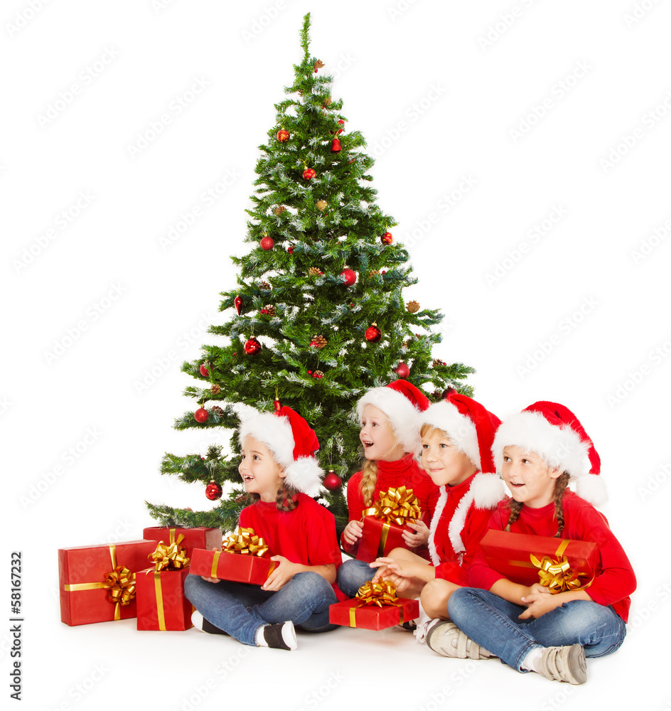 Christmas kids in Santa hat with presents sitting under fir tre Christmas kids in Santa hat with presents sitting under fir tre