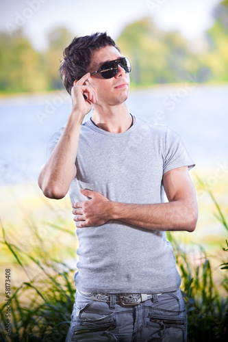 portrait of handsome man in sunglasses posing against lake