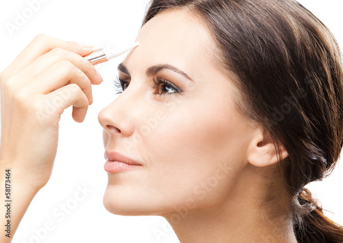 Smiling woman applying concealer on face, isolated