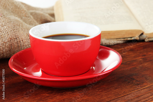 Cup of coffee and book on wooden table on sackcloth background