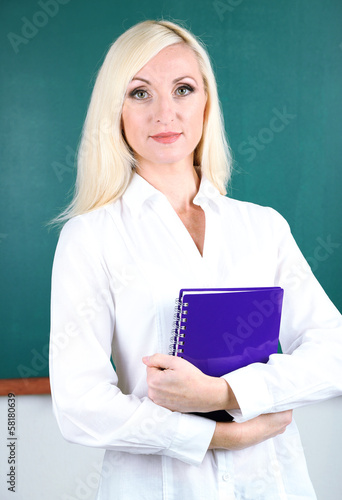 School teacher near blackboard with exercise book in classroom