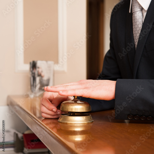 Service bell detail and hand at hotel reception.