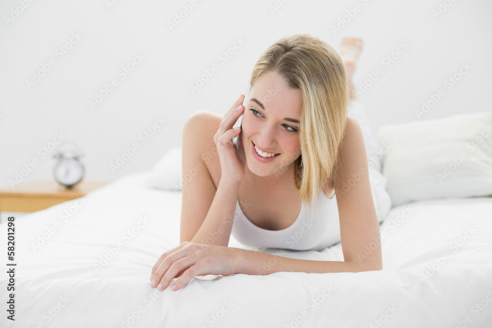 Gleeful lovely woman phoning with her smartphone lying on her be Gleeful lovely woman phoning with her smartphone lying on her be