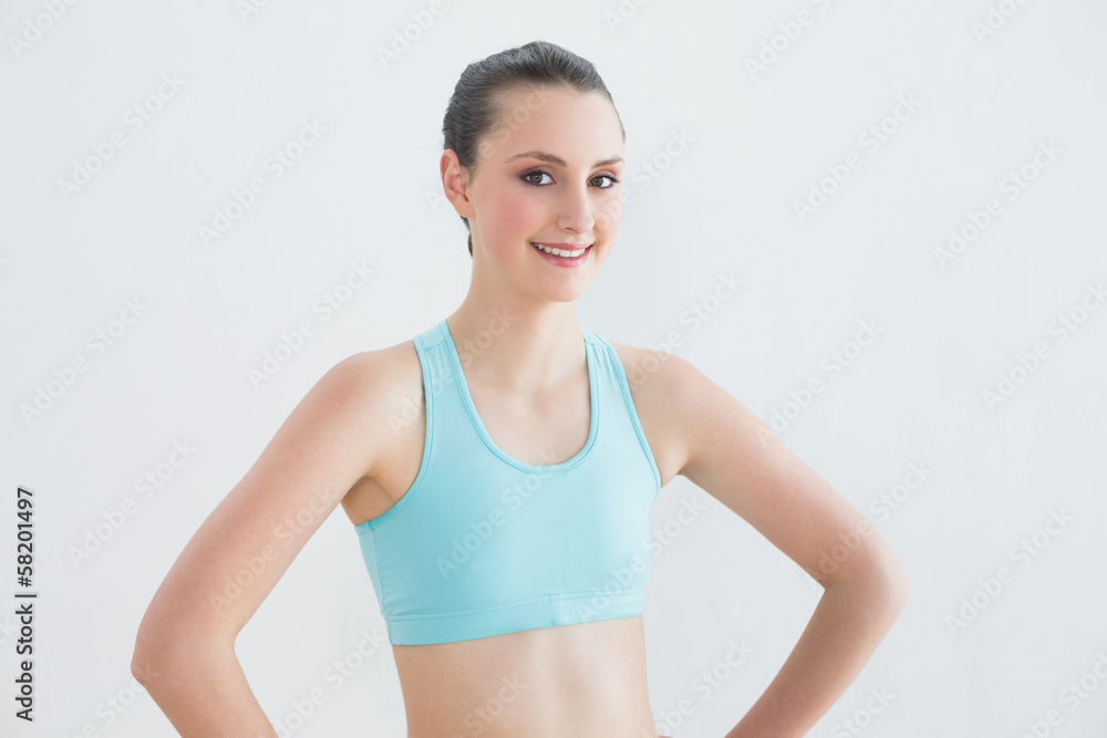 Smiling toned woman with hands on hips against wall