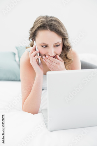 Smiling woman using cellphone and laptop in bed © lightwavemedia