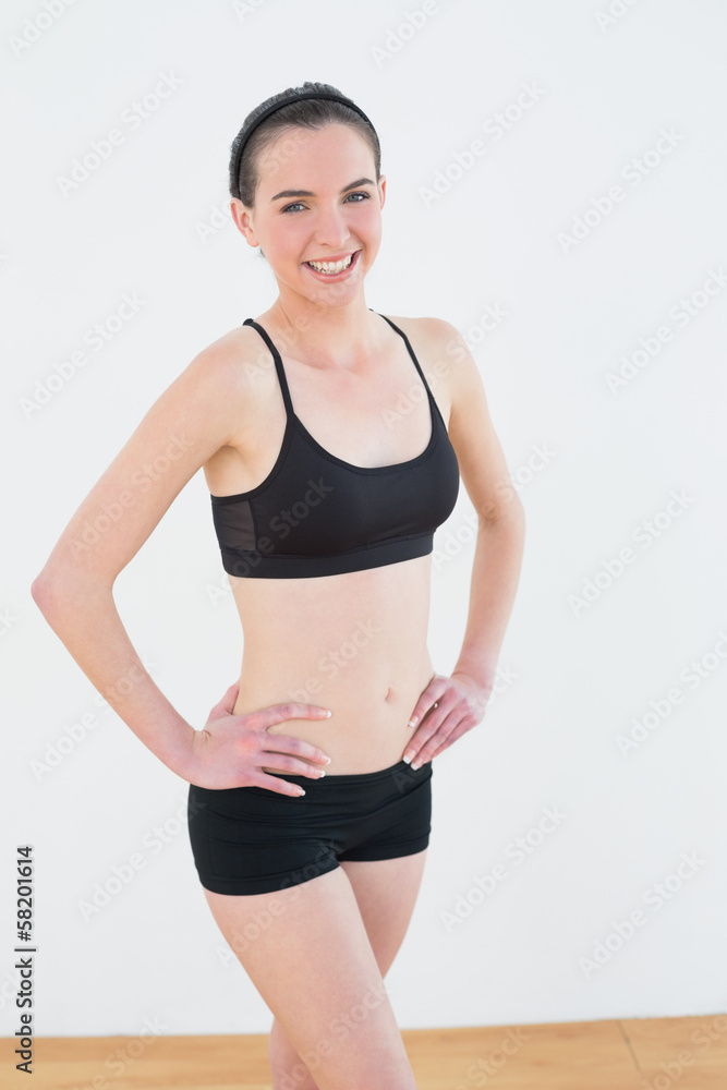 Smiling toned woman with hands on hips in fitness studio