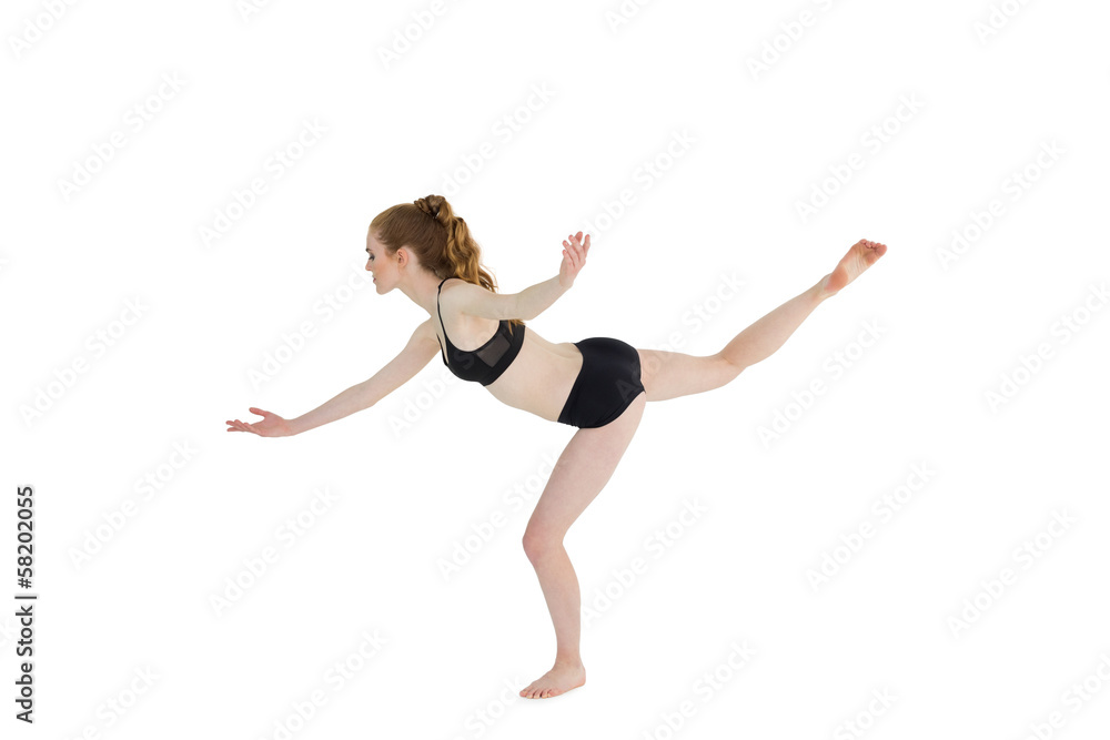 Side view of a sporty young woman standing on one leg