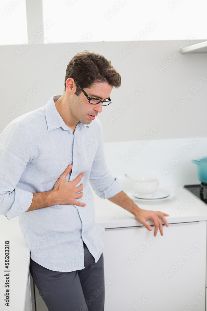 Casual man with stomach pain standing in the kitchen Casual man with stomach pain standing in the kitchen