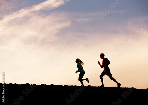 Silhouette of man and woman running jogging together into sunset