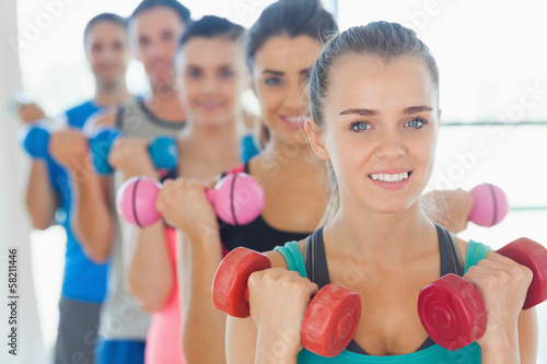 People lifting dumbbell weights with trainer in gym