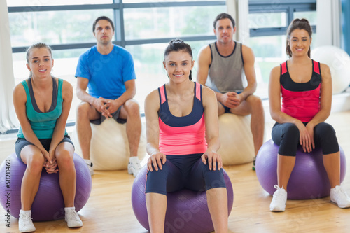 Smiling people sitting on exercise balls in the bright gym