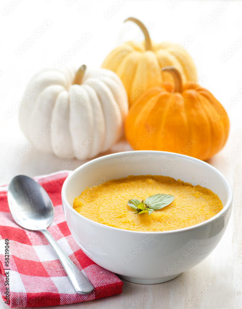 Pumpkin porridge and pumpkins on white wooden table with checker