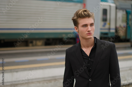 Handsome blond young man with train behind him, in station