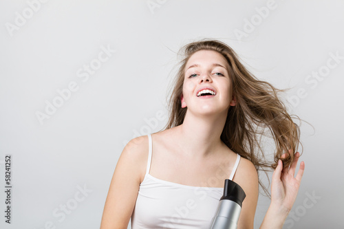 beautiful teenager blow drying her hair and looking at camera