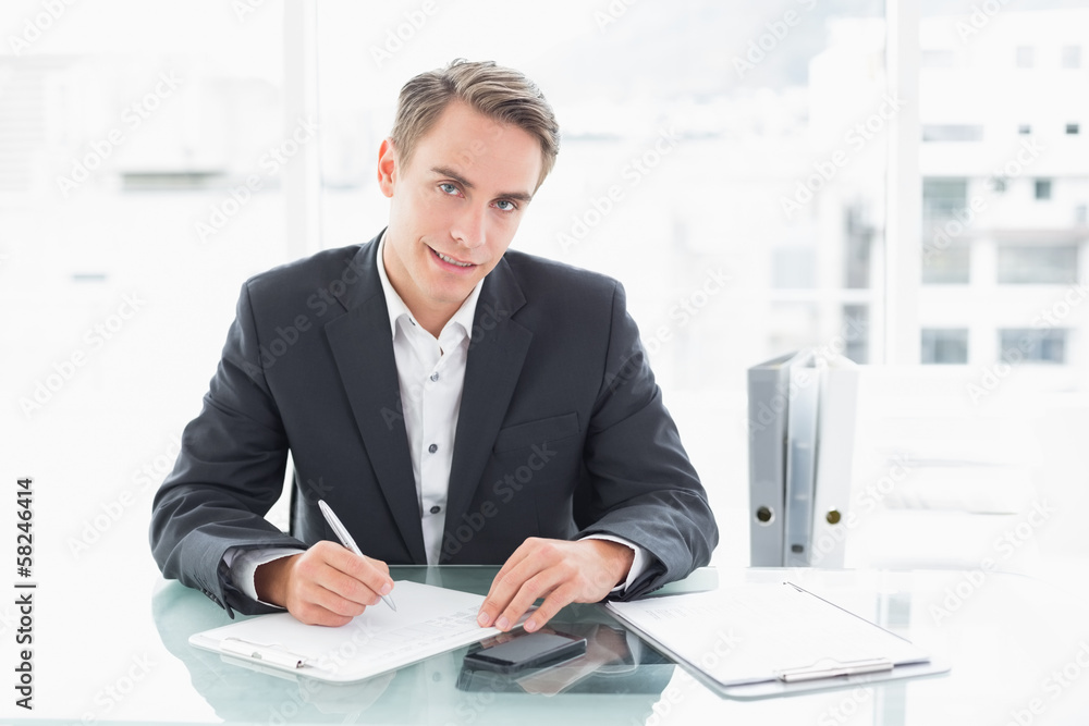 Smiling businessman writing documents at office desk Smiling businessman writing documents at office desk