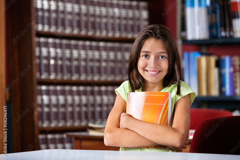 Cute Schoolgirl Holding Book While Sitting In Library