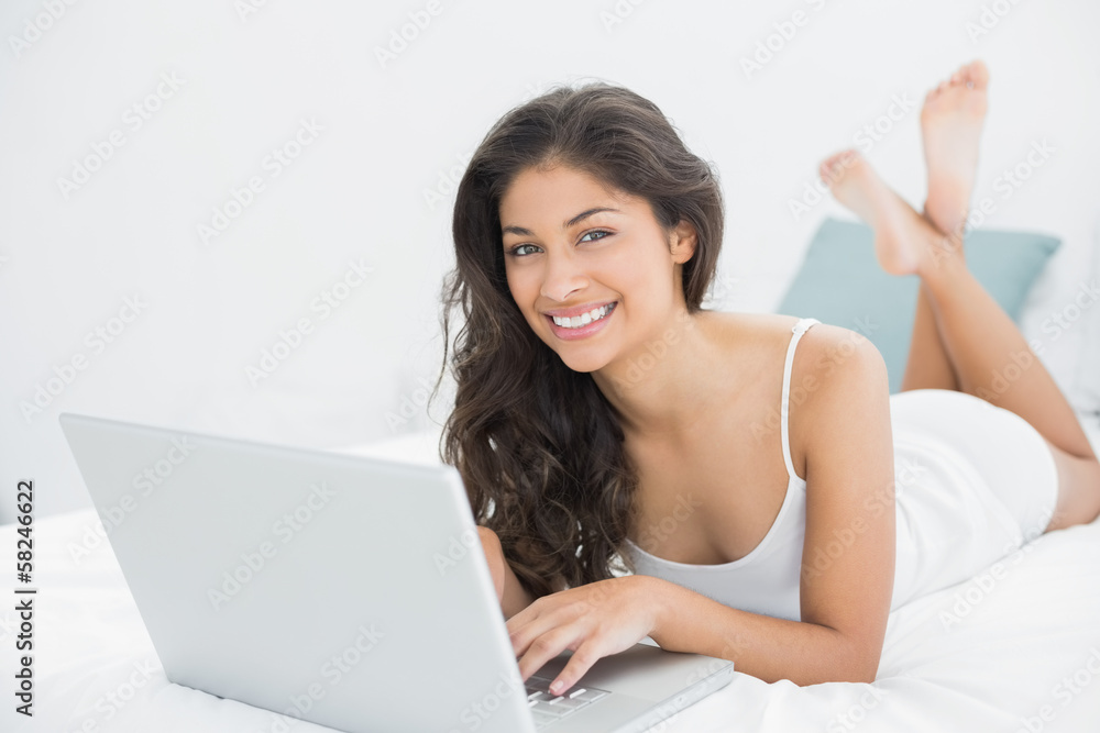 Smiling casual young woman using laptop in bed Smiling casual young woman using laptop in bed