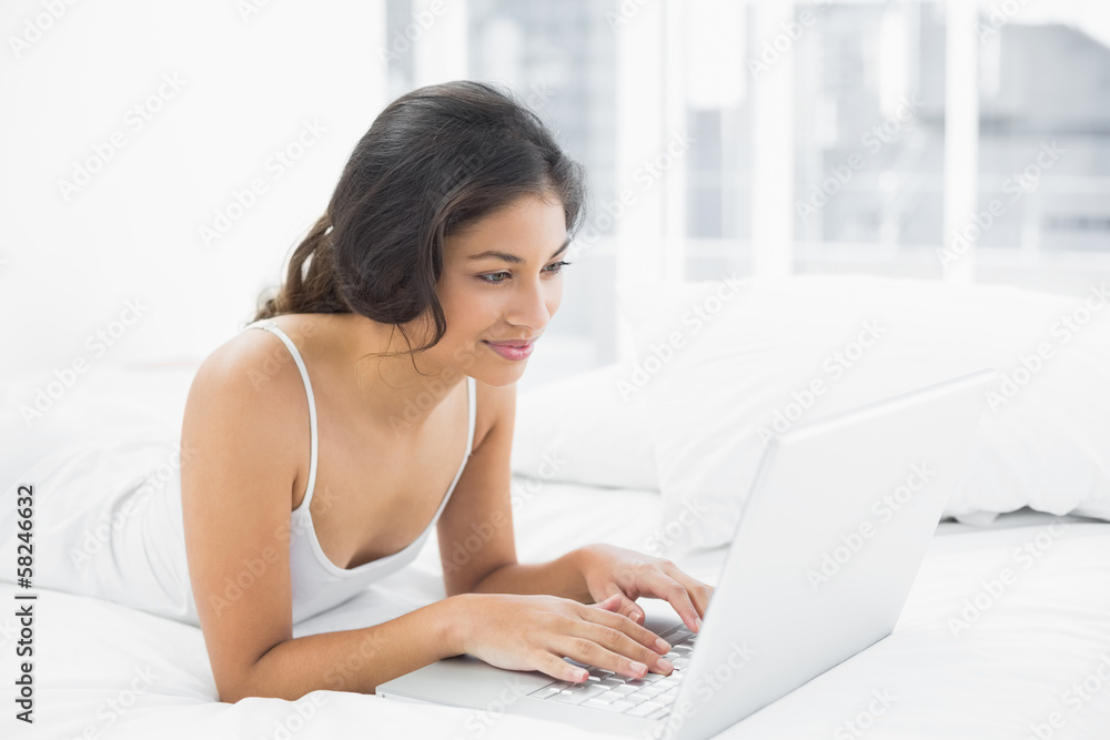 Smiling casual young woman using laptop in bed Smiling casual young woman using laptop in bed