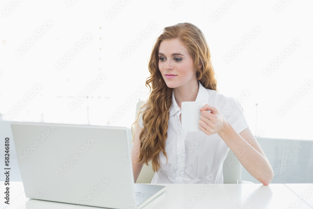Businesswoman drinking coffee while using laptop Businesswoman drinking coffee while using laptop
