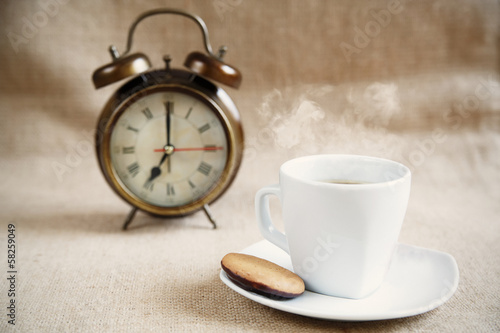A cup of coffee with snack and an alarm clock in the background