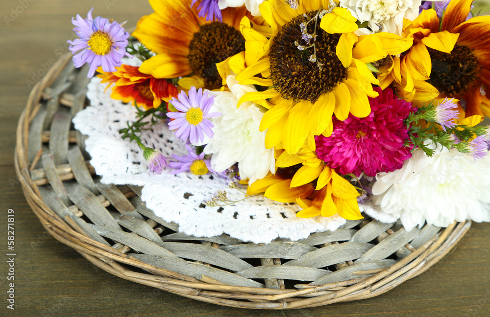 Bouquet of wild flowers on wicker tray on wooden background