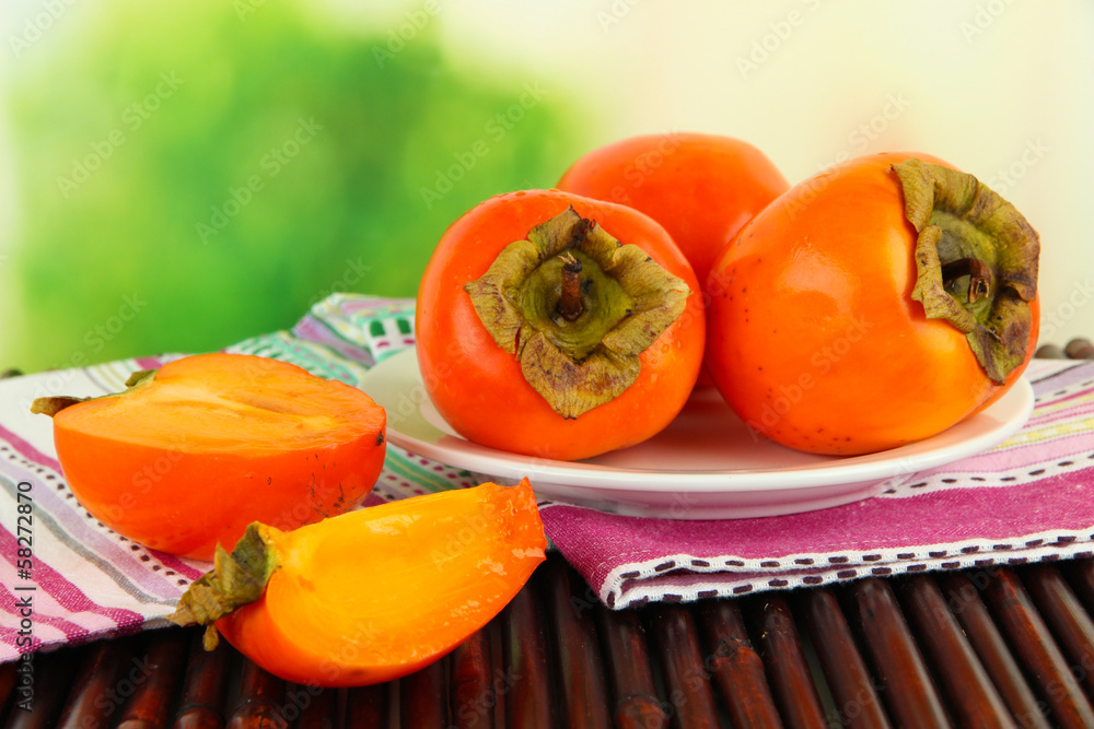 Ripe persimmons on plate on table on bright background Ripe persimmons on plate on table on bright background