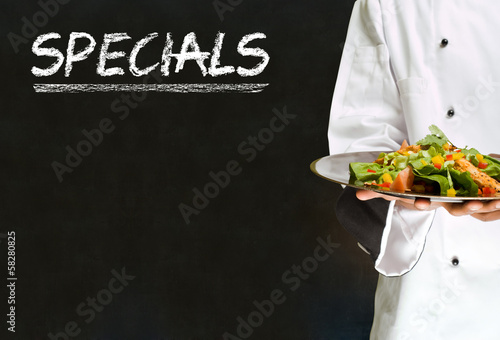 Картината върху платно Chef with chalk specials sign on blackboard background