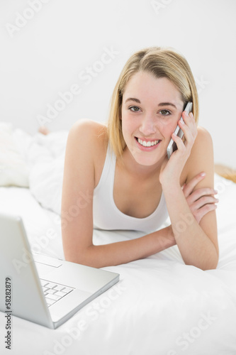 Beautiful blonde woman phoning peacefully lying on her bed