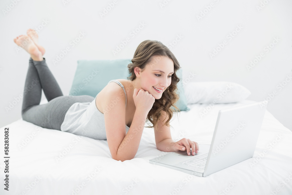 Smiling casual brunette using laptop in bed Smiling casual brunette using laptop in bed