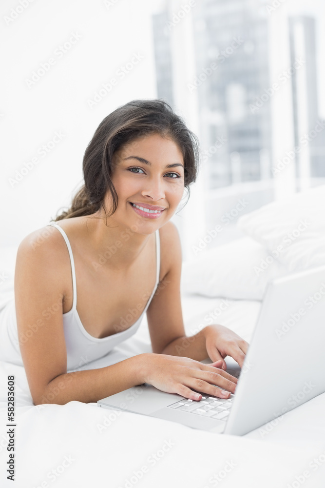 Smiling casual young woman using laptop in bed Smiling casual young woman using laptop in bed