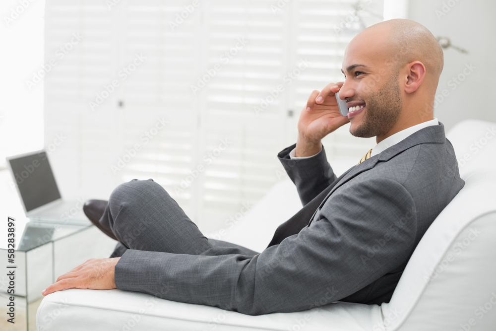 Smiling elegant businessman using cellphone on sofa at home Smiling elegant businessman using cellphone on sofa at home