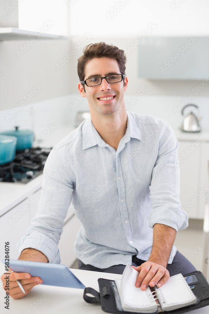 Casual young man with digital tablet and diary in kitchen Casual young man with digital tablet and diary in kitchen