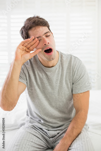 Sleepy man yawning as he rubs his eye in bed