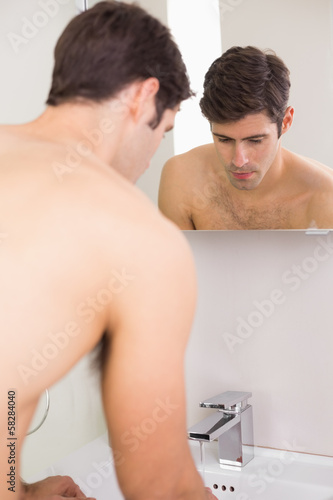 Rear view of tensed shirtless man at washbasin