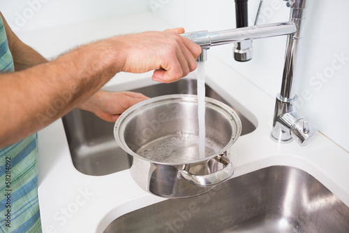 Hands filling pan with water at kitchen sink